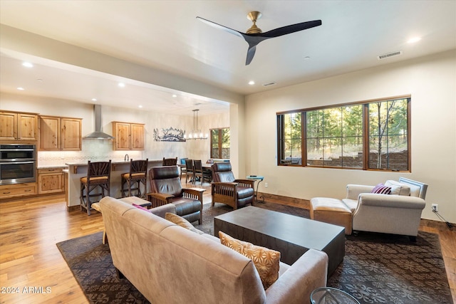 living room with ceiling fan with notable chandelier and light hardwood / wood-style flooring