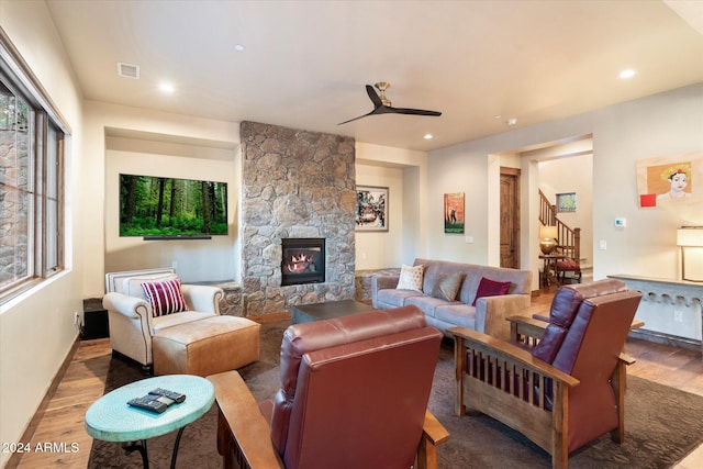 living room with a stone fireplace, ceiling fan, plenty of natural light, and wood-type flooring