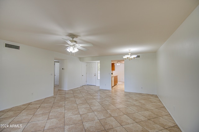 tiled empty room featuring ceiling fan with notable chandelier