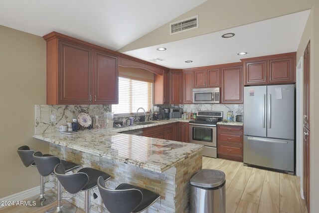 kitchen with kitchen peninsula, appliances with stainless steel finishes, tasteful backsplash, and vaulted ceiling