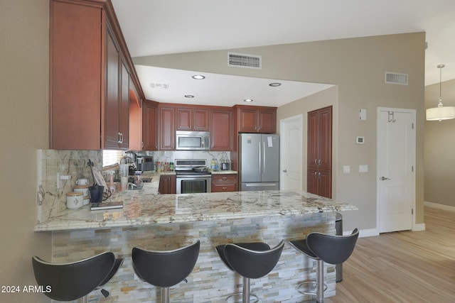 kitchen featuring kitchen peninsula, stainless steel appliances, vaulted ceiling, light hardwood / wood-style floors, and hanging light fixtures