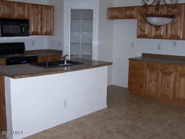 kitchen featuring brown cabinets, black appliances, a center island with sink, a sink, and dark countertops