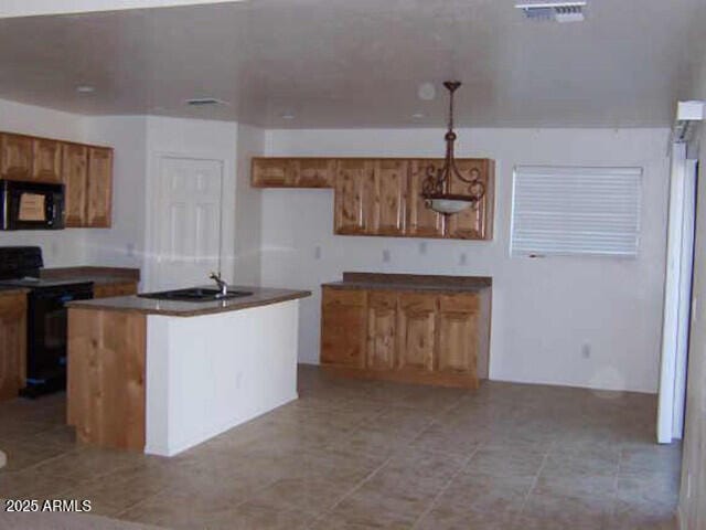 kitchen featuring visible vents, black appliances, a sink, dark countertops, and brown cabinetry