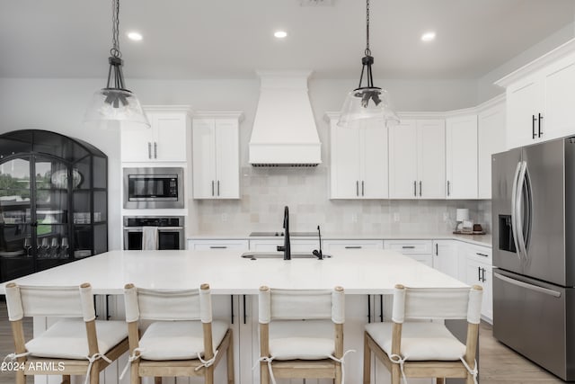 kitchen featuring white cabinets, pendant lighting, stainless steel appliances, and a kitchen island with sink