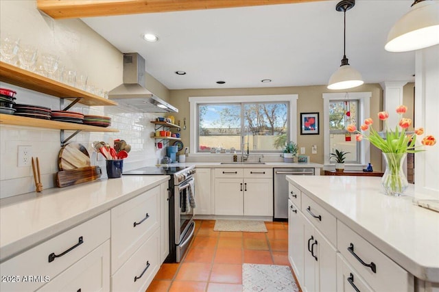 kitchen featuring decorative light fixtures, open shelves, stainless steel appliances, tasteful backsplash, and wall chimney range hood