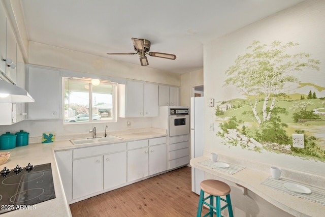 kitchen with a sink, white appliances, light countertops, light wood-style floors, and a ceiling fan