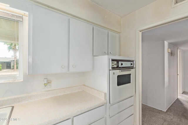 kitchen with white oven, light countertops, and light carpet