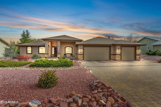 prairie-style house featuring a garage, stucco siding, decorative driveway, and stone siding
