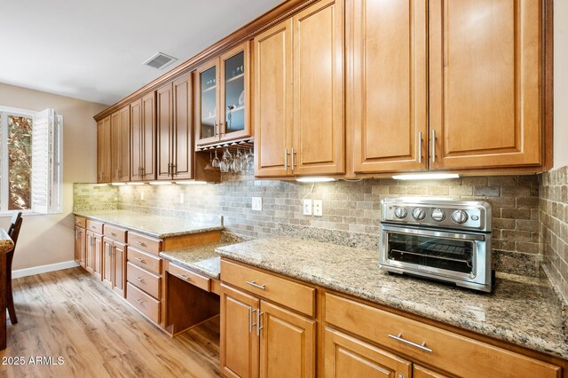 kitchen featuring a toaster, light stone counters, light wood finished floors, and visible vents