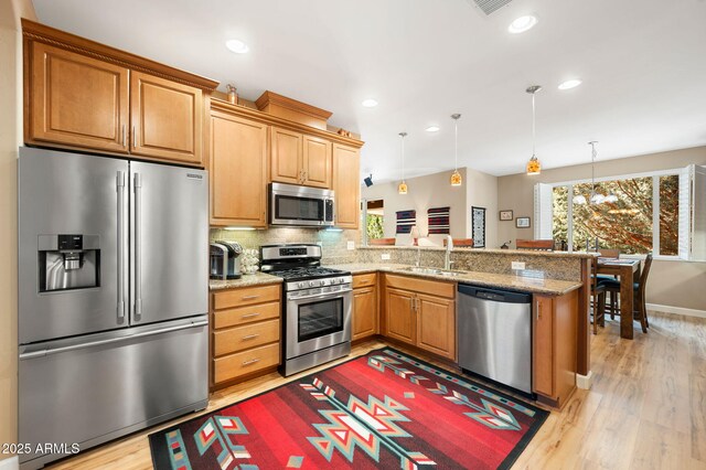 kitchen with a peninsula, a sink, light wood-style flooring, decorative light fixtures, and stainless steel appliances
