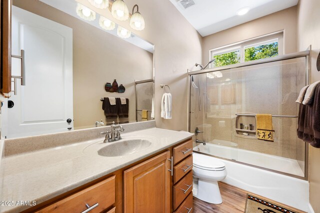 bathroom with visible vents, wood finished floors, vanity, toilet, and shower / bath combination with glass door