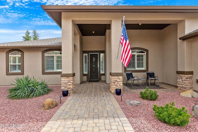 property entrance with a porch, stucco siding, and stone siding