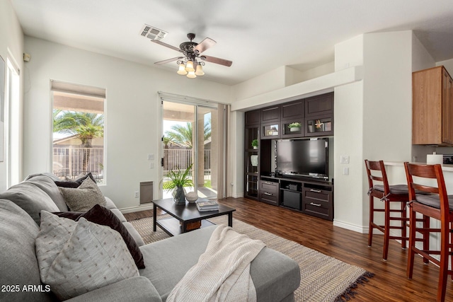 living area with dark wood-type flooring, a ceiling fan, visible vents, and baseboards