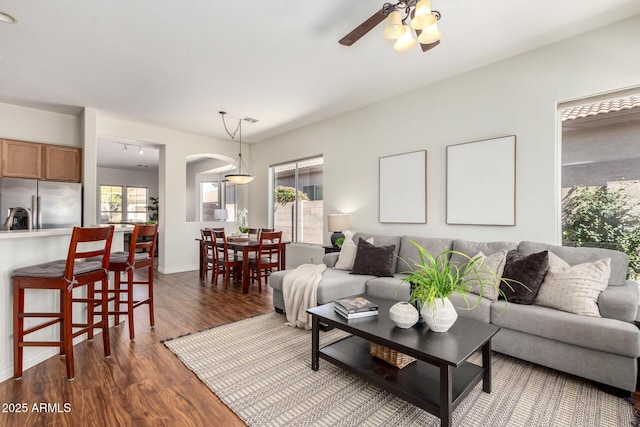 living area featuring ceiling fan, dark wood-type flooring, baseboards, and a healthy amount of sunlight