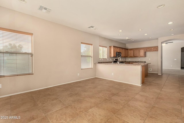 kitchen featuring arched walkways, light stone counters, visible vents, baseboards, and stainless steel microwave