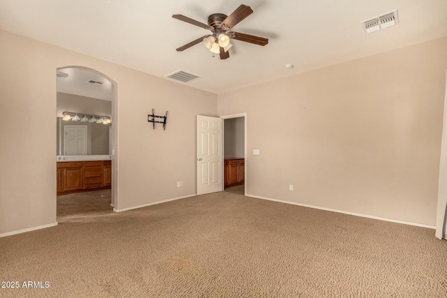 spare room featuring arched walkways, visible vents, ceiling fan, and light carpet