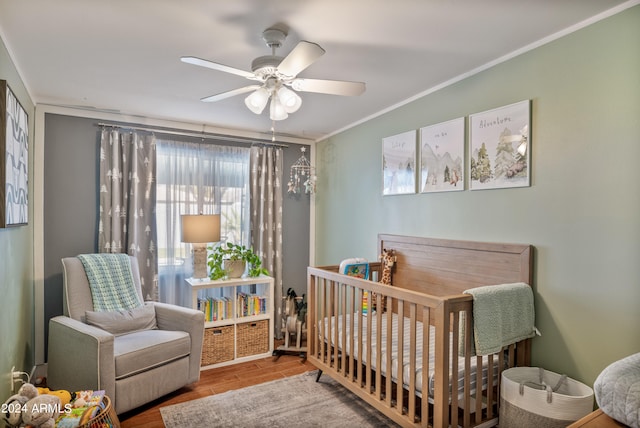 bedroom with a crib, light wood-type flooring, crown molding, and ceiling fan