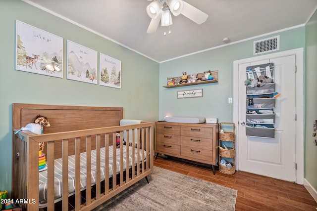 bedroom featuring wood-type flooring, ceiling fan, a nursery area, and crown molding