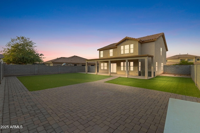 back house at dusk with a patio area and a lawn