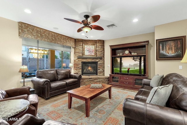 living room with a fireplace, light wood-type flooring, and ceiling fan