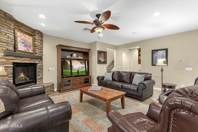 living room featuring a stone fireplace, ceiling fan, and light hardwood / wood-style floors