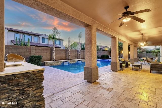 pool at dusk with ceiling fan, a patio area, and exterior bar