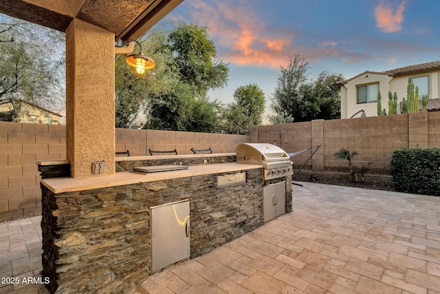 patio terrace at dusk featuring area for grilling and exterior kitchen