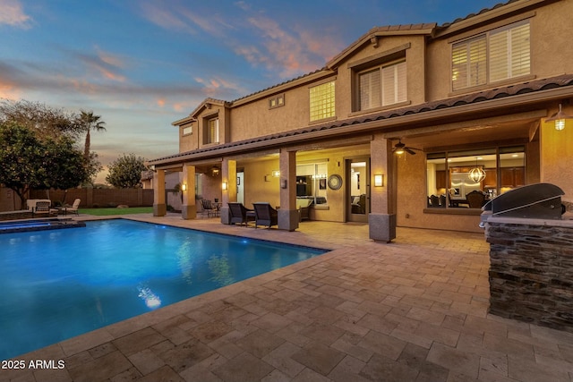 pool at dusk featuring an in ground hot tub, exterior kitchen, and a patio