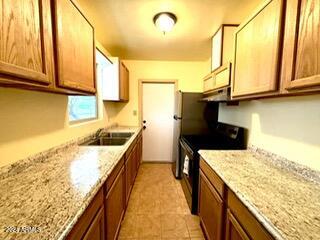 kitchen featuring light stone countertops, black electric range oven, extractor fan, and sink