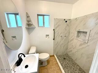 bathroom with tiled shower, plenty of natural light, vanity, and toilet