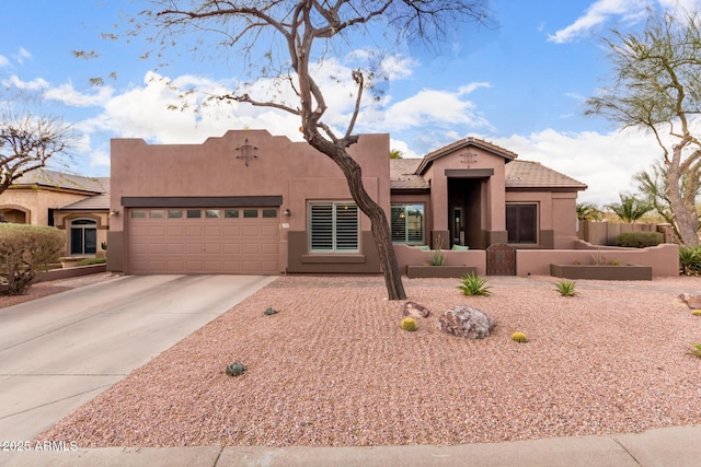 pueblo-style house featuring a garage, concrete driveway, a fenced front yard, a tiled roof, and stucco siding