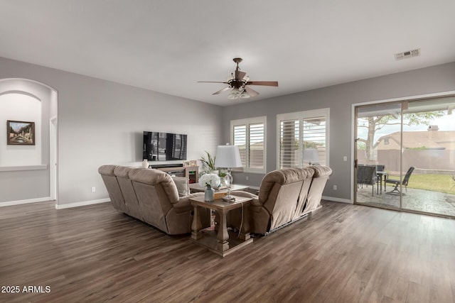 living room featuring dark wood-style floors, arched walkways, visible vents, ceiling fan, and baseboards