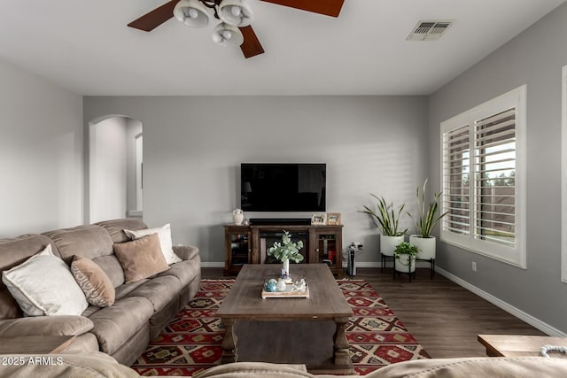 living area with arched walkways, visible vents, ceiling fan, wood finished floors, and baseboards