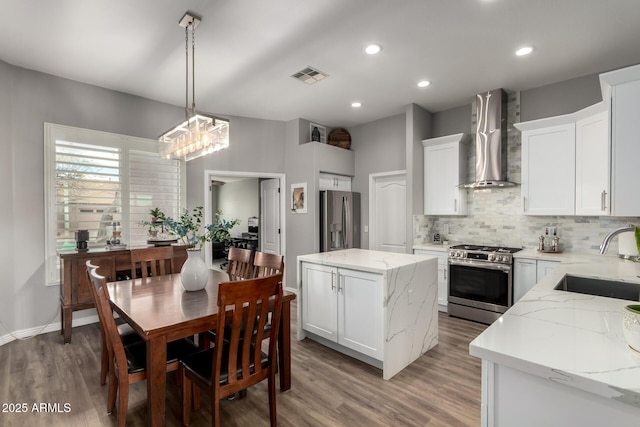 kitchen featuring stainless steel appliances, a sink, visible vents, backsplash, and wall chimney exhaust hood