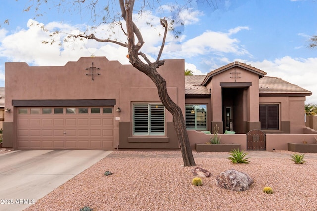 pueblo-style house with stucco siding, concrete driveway, an attached garage, a gate, and fence