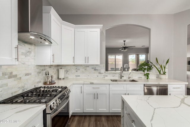 kitchen featuring white cabinets, wall chimney exhaust hood, appliances with stainless steel finishes, a sink, and backsplash