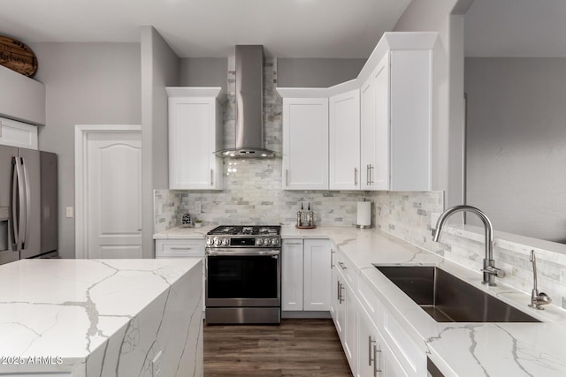 kitchen with stainless steel appliances, tasteful backsplash, white cabinets, a sink, and wall chimney exhaust hood