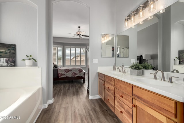 ensuite bathroom with double vanity, a ceiling fan, a sink, ensuite bath, and wood finished floors