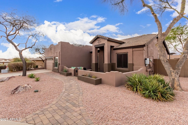 pueblo-style house featuring a garage, a tile roof, fence, and stucco siding