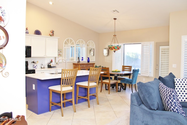 kitchen with pendant lighting, a breakfast bar, light tile patterned floors, a kitchen island with sink, and white cabinets