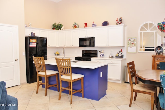 kitchen with black appliances, white cabinets, a kitchen island with sink, and light tile patterned flooring