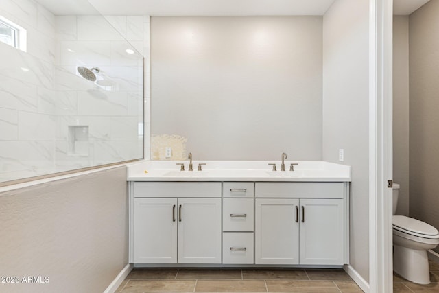 bathroom with double vanity, a tile shower, a sink, and toilet