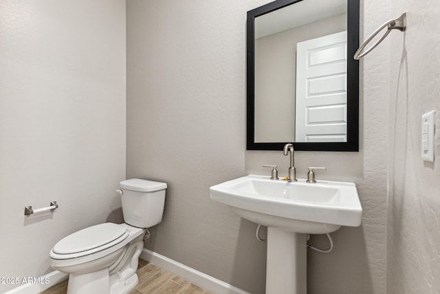 half bathroom with toilet, wood finished floors, and baseboards