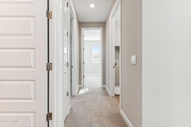 hall featuring baseboards and light colored carpet
