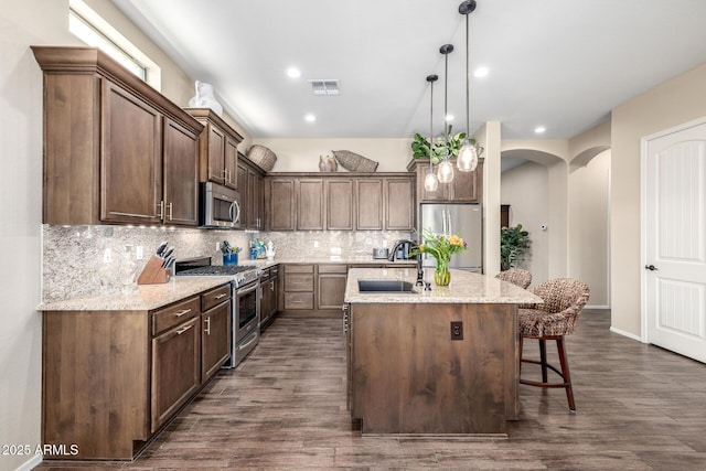1822 N Waverly, Mesa, AZ 85207 - kitchen featuring appliances with stainless steel finishes, a kitchen island with sink, tasteful backsplash, dark wood-style flooring, and a kitchen breakfast bar