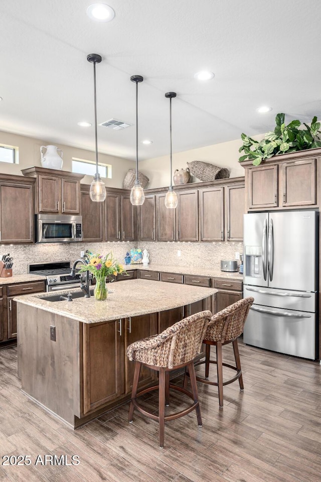 1822 N Waverly, Mesa, AZ 85207 - kitchen featuring stainless steel appliances, decorative backsplash, an island with sink, light stone countertops, and a kitchen bar