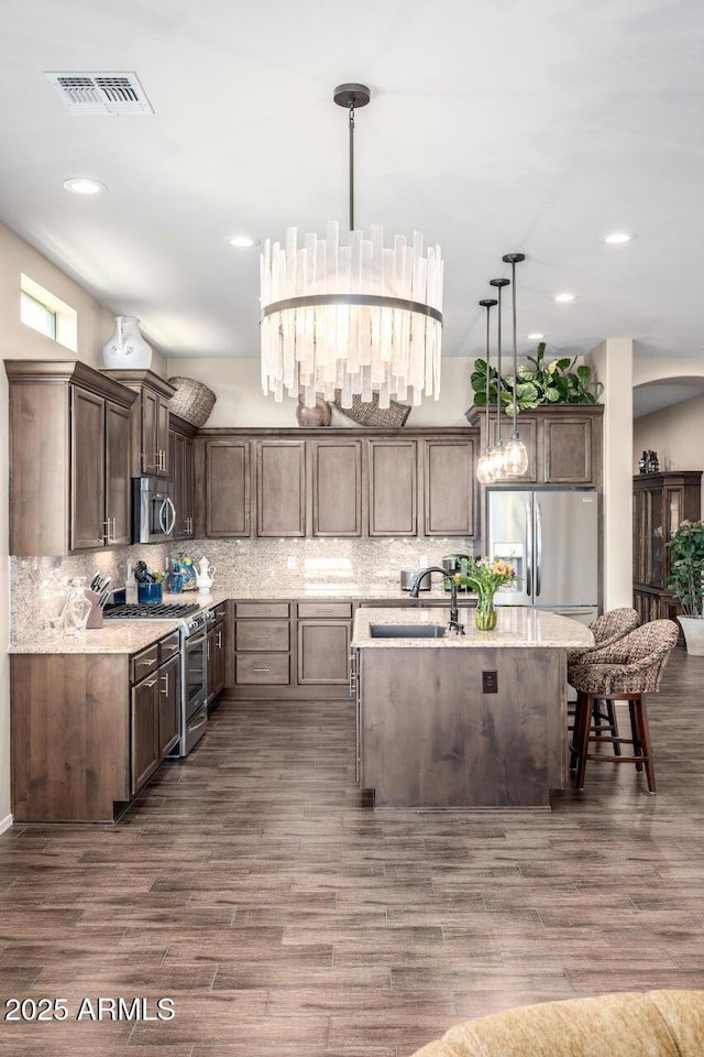 1822 N Waverly, Mesa, AZ 85207 - kitchen featuring stainless steel appliances, dark wood-style floors, a kitchen island with sink, tasteful backsplash, and decorative light fixtures