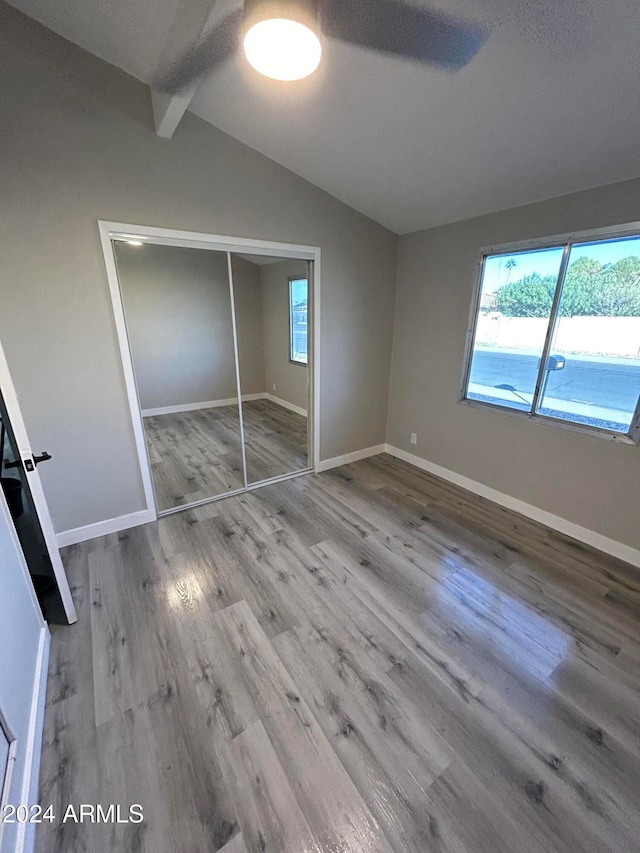 unfurnished bedroom featuring hardwood / wood-style flooring, vaulted ceiling with beams, a textured ceiling, and a closet