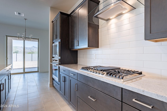 kitchen featuring light stone counters, hanging light fixtures, a mountain view, stainless steel appliances, and wall chimney range hood