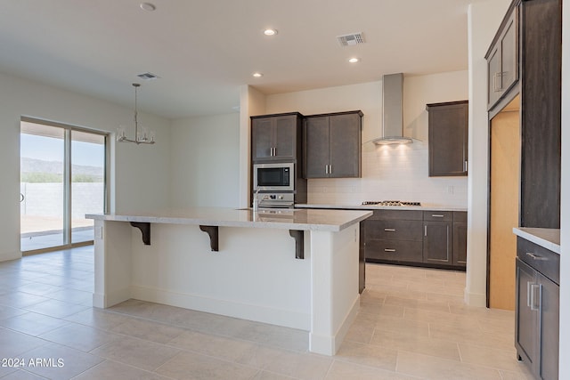 kitchen featuring wall chimney exhaust hood, a breakfast bar area, tasteful backsplash, appliances with stainless steel finishes, and a kitchen island with sink